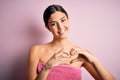 Young beautiful girl wearing towel shower after bath standing over isolated pink background smiling in love showing heart symbol