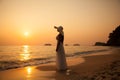 Young beautiful girl in a white dress and straw hat on a tropical beach at sunset. Summer vacation concept. Royalty Free Stock Photo