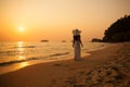 Young beautiful girl in a white dress and straw hat on a tropical beach at sunset. Summer vacation concept. Royalty Free Stock Photo