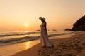 Young beautiful girl in a white dress and straw hat on a tropical beach at sunset. Summer vacation concept. Royalty Free Stock Photo