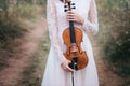 Young beautiful girl in a white dress under tree holding a violin in hands.