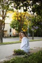 Young beautiful girl in a white shirt and black pant sitting near blooming lilac trees with purple flowers outdoors, flowering Royalty Free Stock Photo