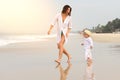 A young beautiful girl in a white shirt runs along a sandy beach in the sea with her son in white clothes and hat Royalty Free Stock Photo