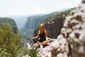 Young beautiful girl woman in black sporty slim outfit meditating on edge rock mountain cliff peak with view on valley Royalty Free Stock Photo