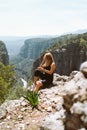 Young beautiful girl woman in black sporty slim outfit sitting on edge rock mountain cliff peak with view on valley Royalty Free Stock Photo