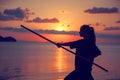 Young beautiful girl woman blond doing kung fu with bamboo stick on the seashore at sunset, fight Royalty Free Stock Photo