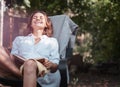 Young beautiful girl woman enjoys nature and reading a book in the summer in the garden of her house sitting on a chair Royalty Free Stock Photo