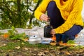 Young beautiful girl in a yellow sweater makes coffee in the forest on a gas burner. Making coffee on a primus stove in the autumn