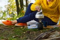 Young beautiful girl in a yellow sweater makes coffee in the forest on a gas burner. Making coffee on a primus stove in the autumn