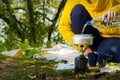 Young beautiful girl in a yellow sweater makes coffee in the forest on a gas burner. Making coffee on a primus stove in the autumn