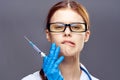 Young beautiful in glasses and in medical clothes holds a syringe on a dark gray background, portrait Royalty Free Stock Photo