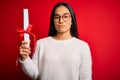 Young beautiful graduate asian woman holding university degree diploma over red background with a confident expression on smart Royalty Free Stock Photo