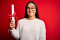 Young beautiful graduate asian woman holding university degree diploma over red background with a happy face standing and smiling Royalty Free Stock Photo