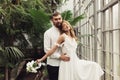 Young beautiful groom in shirt and gorgeous bride in white dress with little bouquet of flowers in hand dreamily looking Royalty Free Stock Photo