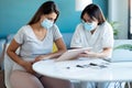 Young beautiful gynecologist wearing a hygienic face mask while showing to pregnant woman ultrasound scan baby with digital tablet