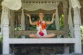 Young beautiful and happy American tourist woman practicing yoga and meditation sitting in lotus position at outdoors hut enjoying Royalty Free Stock Photo