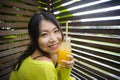 Young attractive and happy Asian Chinese girl having fun in garden outdoors drinking healthy orange juice with straw playful Royalty Free Stock Photo