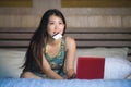 Young beautiful happy Asian Chinese girl using credit card internet banking on laptop computer at home in bed smiling shopping onl Royalty Free Stock Photo