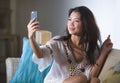 Young beautiful and happy Asian Chinese 20s or 30s woman taking selfie picture with mobile phone sitting at home living room sofa Royalty Free Stock Photo