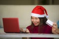 Young beautiful and happy Asian Chinese woman in Christmas Santa Claus hat holding credit card using laptop computer for internet Royalty Free Stock Photo