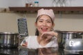 Young beautiful and happy Asian Chinese woman in head scarf at home kitchen smiling happy and relaxed enjoying cooking looking at Royalty Free Stock Photo