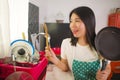 Young beautiful and happy Asian Chinese woman in kitchen apron holding spoon and cooking pan smiling cheerful enjoying domestic Royalty Free Stock Photo