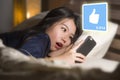 Young beautiful and happy Asian Chinese woman in pajamas using mobile phone social media excited and surprised lying on bed at
