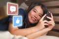 Young beautiful and happy Asian Chinese woman in pajamas using mobile phone social media smiling cheerful lying on bed at home Royalty Free Stock Photo