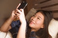 Young beautiful and happy Asian Chinese woman in pajamas using mobile phone social media texting with her boyfriend or enjoying Royalty Free Stock Photo