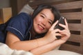 Young beautiful and happy Asian Chinese woman in pajamas using mobile phone social media texting with her boyfriend or enjoying Royalty Free Stock Photo