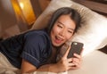 Young beautiful and happy Asian Chinese woman in pajamas using mobile phone social media texting with her boyfriend or enjoying Royalty Free Stock Photo