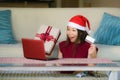 Young beautiful and happy Asian Chinese woman in Santa hat holding credit card and Christmas present box using laptop computer for Royalty Free Stock Photo