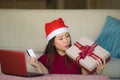 Young beautiful and happy Asian Chinese woman in Santa hat holding credit card and Christmas present box using laptop computer for Royalty Free Stock Photo