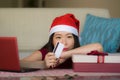 Young beautiful and happy Asian Chinese woman in Santa hat holding credit card and Christmas present box using laptop computer for Royalty Free Stock Photo