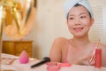 Young beautiful and happy Asian Chinese woman with towel head wrap applying makeup looking to mirror smiling cheerful preparing Royalty Free Stock Photo