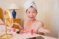 Young beautiful and happy Asian Chinese woman with towel head wrap applying makeup looking to mirror smiling cheerful preparing Royalty Free Stock Photo