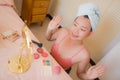 Young beautiful and happy Asian Chinese woman with towel head wrap applying makeup looking to mirror smiling cheerful preparing Royalty Free Stock Photo