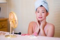 Young beautiful and happy Asian Chinese woman with towel head wrap applying makeup looking to mirror smiling cheerful preparing Royalty Free Stock Photo