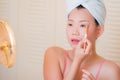 Young beautiful and happy Asian Chinese woman with towel head wrap applying makeup looking to mirror smiling cheerful preparing Royalty Free Stock Photo