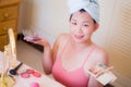 Young beautiful and happy Asian Chinese woman with towel head wrap applying makeup looking to mirror smiling cheerful preparing Royalty Free Stock Photo