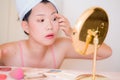 Young beautiful and happy Asian Chinese woman with towel head wrap applying makeup looking to mirror smiling cheerful preparing Royalty Free Stock Photo