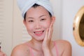 Young beautiful and happy Asian Chinese woman with towel head wrap applying makeup looking to mirror smiling cheerful preparing Royalty Free Stock Photo