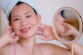 Young beautiful and happy Asian Chinese woman with towel head wrap applying makeup looking to mirror smiling cheerful preparing Royalty Free Stock Photo