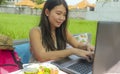 Young beautiful and happy Asian Chinese woman working outdoors with laptop computer networking green grass background cafe as digi Royalty Free Stock Photo