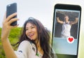 Young beautiful and happy Asian Chinese woman using internet online dating app on mobile phone sending like message to handsome Ca Royalty Free Stock Photo