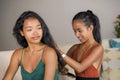 Young beautiful and happy Asian girlfriends at home couch with one girl brushing the hair of the other woman