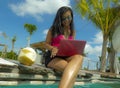 Young beautiful and happy Asian Indonesian teenager woman in bikini at tropical resort swimming pool networking relaxed and Royalty Free Stock Photo