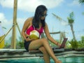 Young beautiful and happy Asian Indonesian teenager woman in bikini at tropical resort swimming pool networking relaxed and Royalty Free Stock Photo