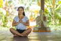 Young beautiful and happy Asian Indonesian woman with Balinese style ear flower sitting on wood floor in lotus pose meditating Royalty Free Stock Photo