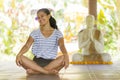 Young beautiful and happy Asian Indonesian woman with Balinese style ear flower sitting on wood floor in lotus pose smiling at Royalty Free Stock Photo